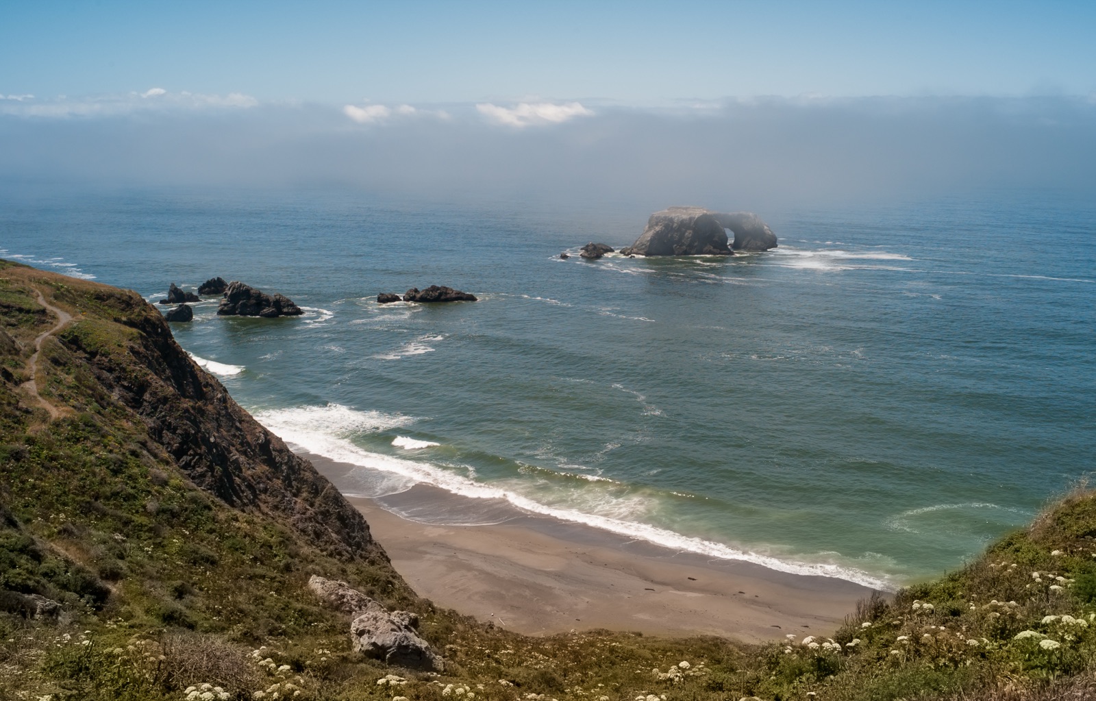 Marine-layer fog pouring over the Arched Rock sea stack on the Sonoma Coast