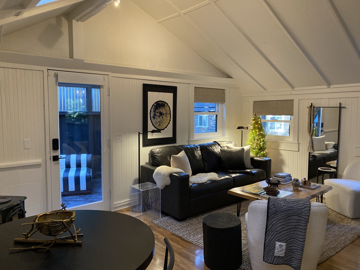 The sitting room under a vaulted white ceiling — black leather sofa with sheepskin throw, tree-ring art, wood coffee table and a lit little tree in the corner