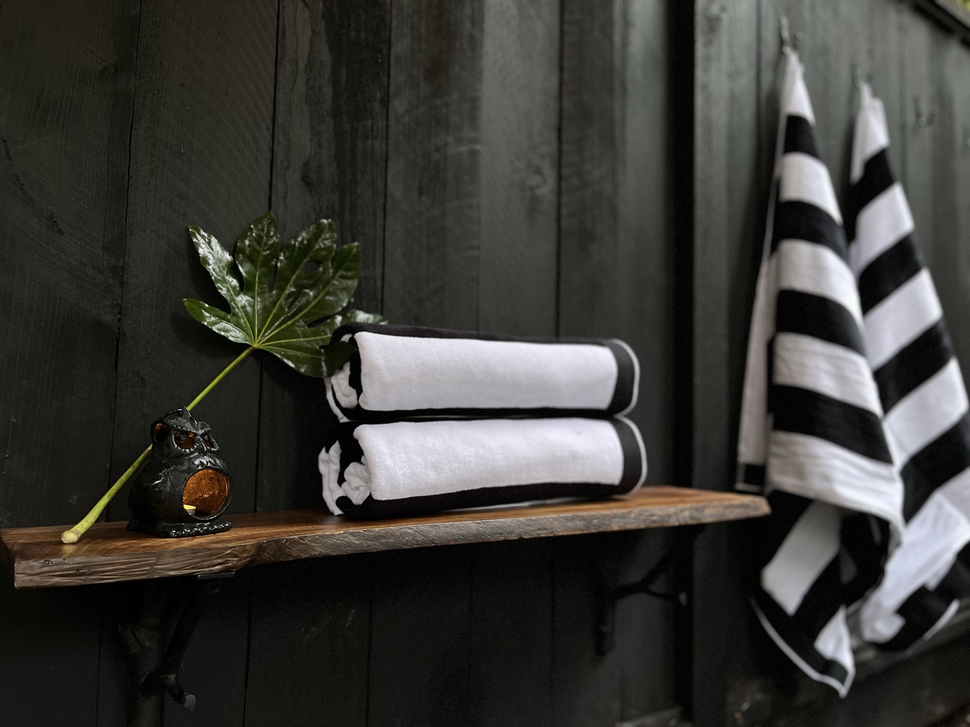 Folded black-and-white striped towels on a live-edge wood shelf with a small owl candle, more towels hanging on hooks against the black wall